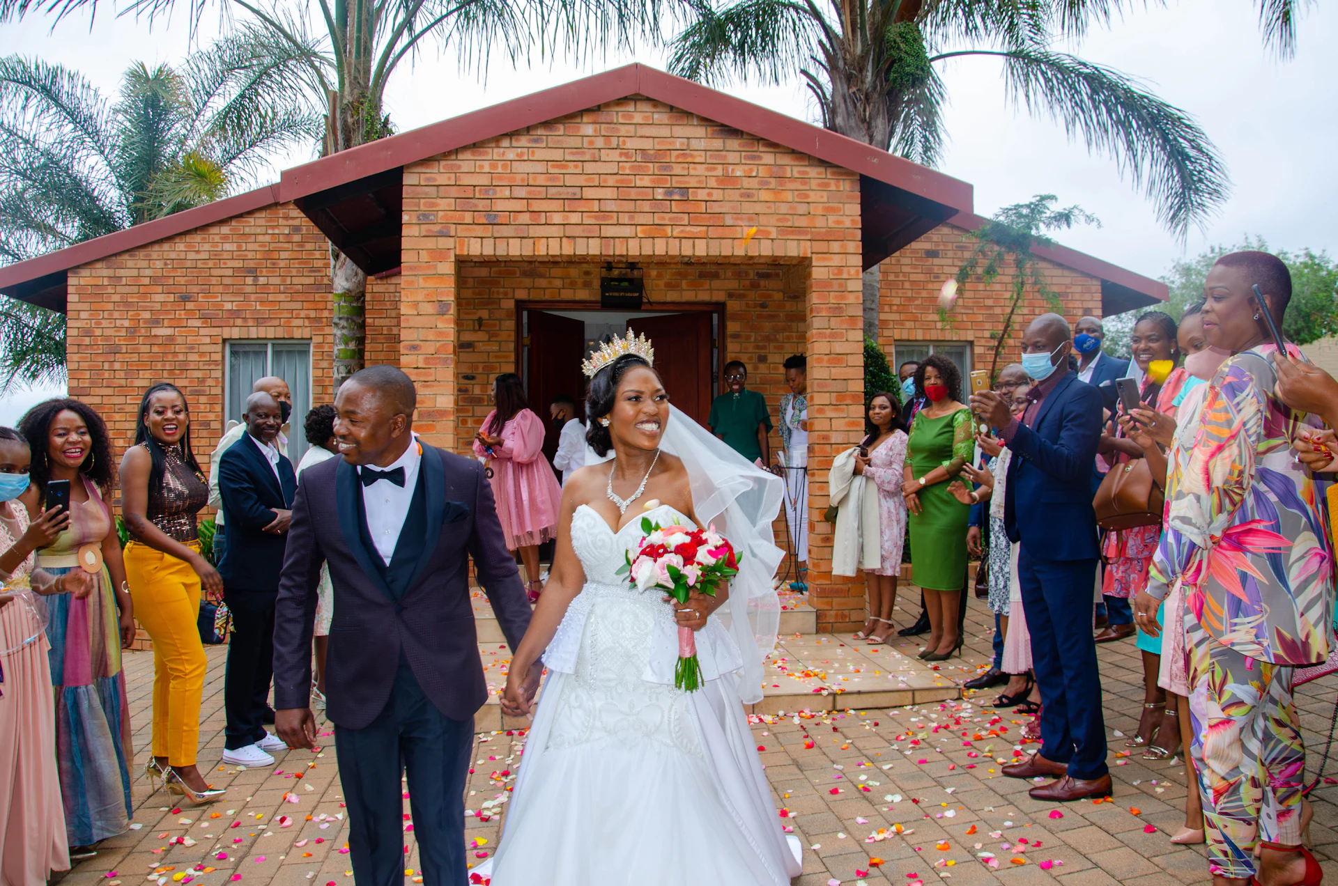 A bride and groom walk out past their cheering guests