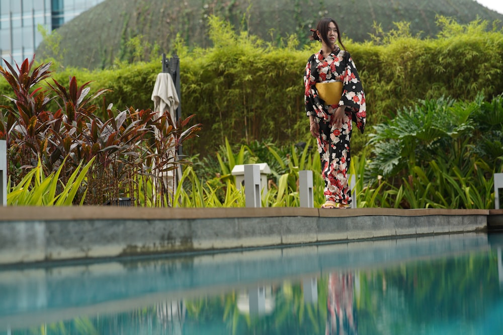 woman in black and white floral dress standing beside swimming pool during daytime