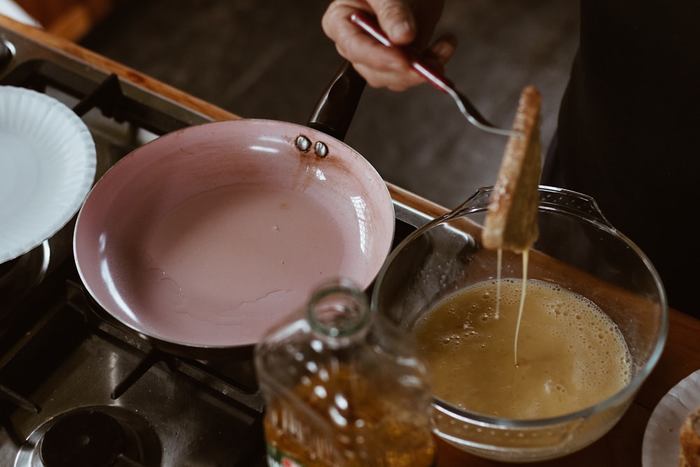 pessoa segurando colher de aço inoxidável derramando líquido marrom na xícara de chá de cerâmica branca