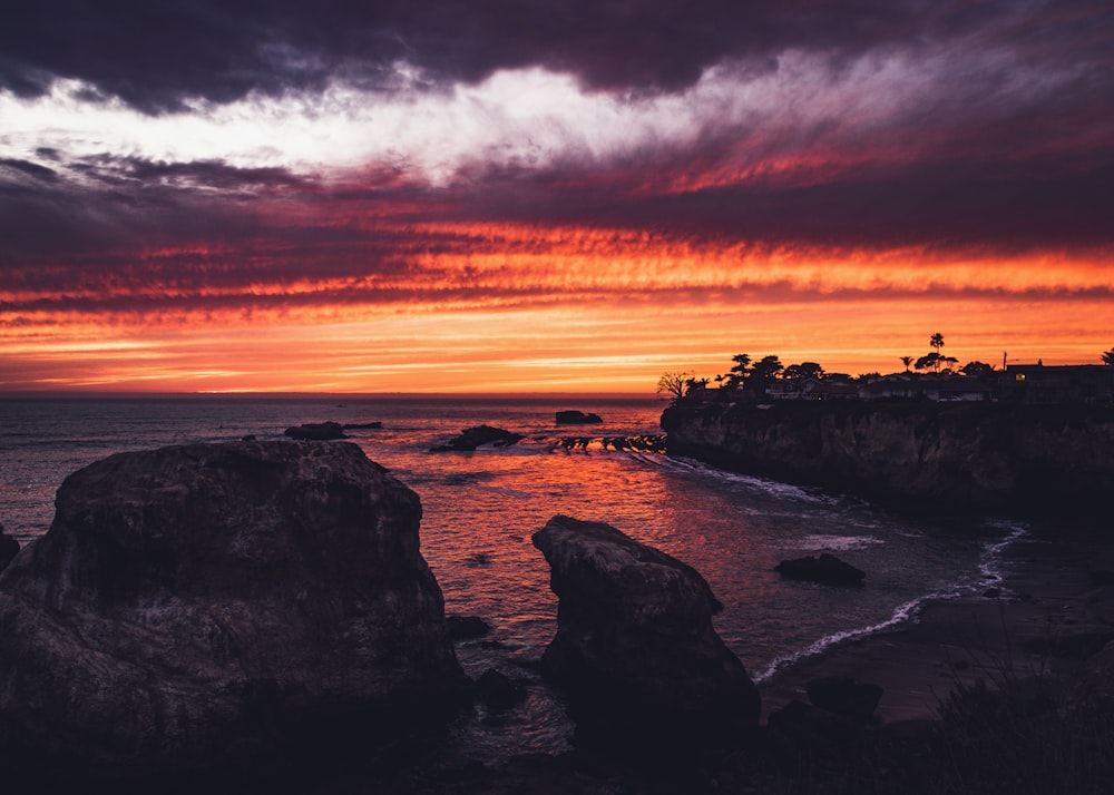 silhouette of rocks on sea shore during sunset