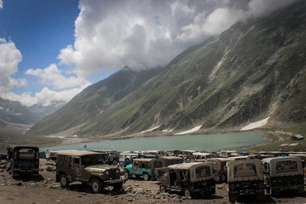 A convoy of SUVs and tempo travellers parked beside a serene lake in Leh Ladakh.