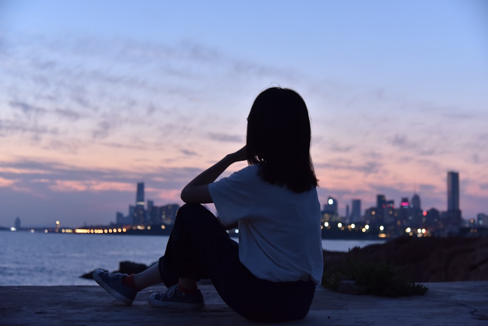 mulher na camisa branca sentada no chão durante o pôr do sol