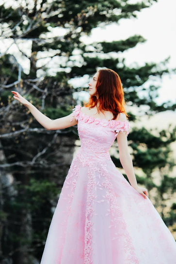A stylish woman wearing a flowing dress in a soft pink setting.