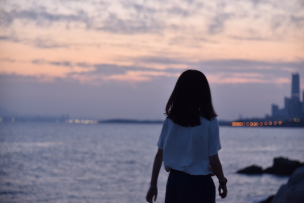 Frau im weißen Hemd steht bei Sonnenuntergang am Meeresufer