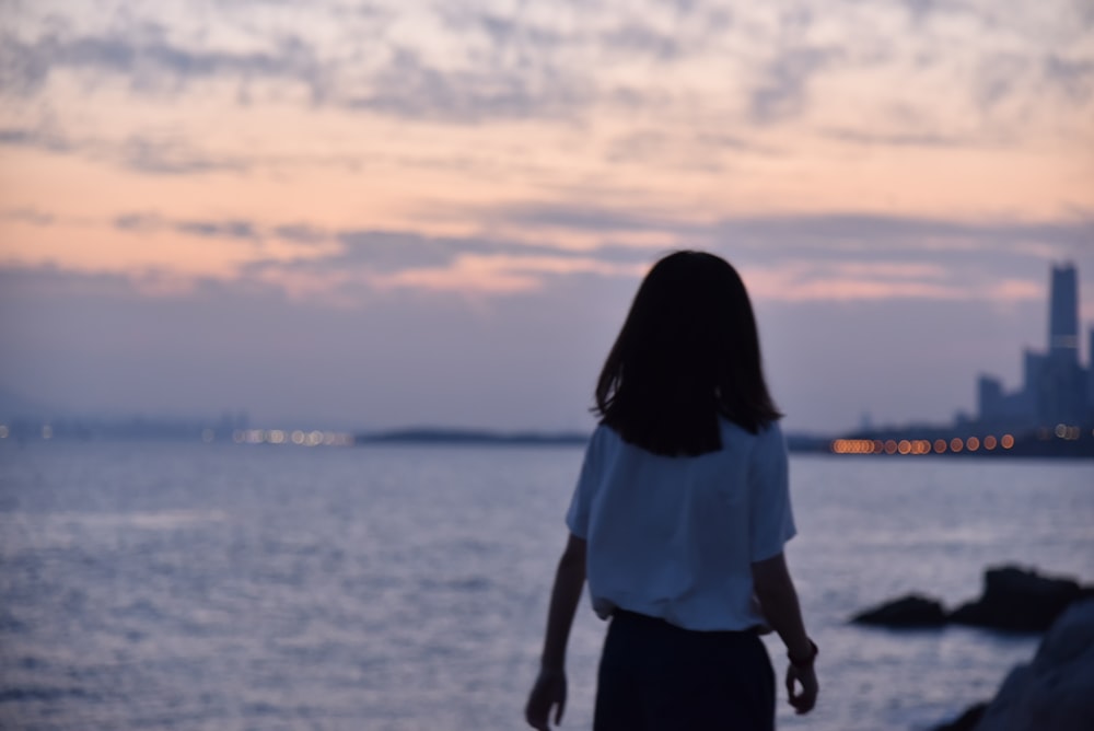 femme en chemise blanche debout sur le bord de mer au coucher du soleil