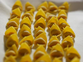 Close-up of handmade tortellini arranged on a rustic wooden board.