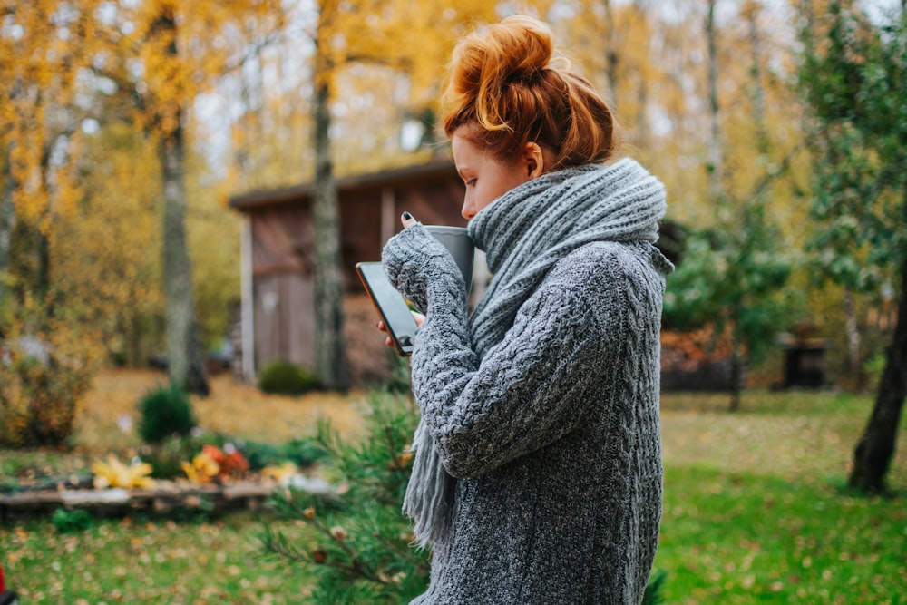 woman in gray scarf and gray sweater standing on green grass field during daytime