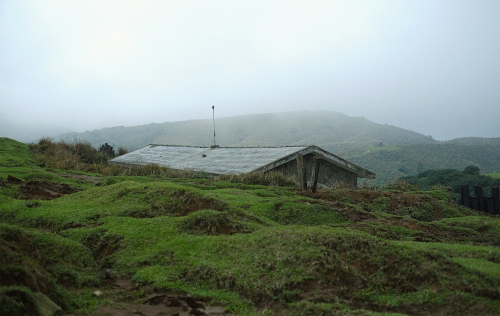 brown wooden house on green grass field near mountain under white sky during daytime