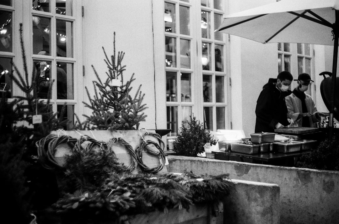 grayscale photo of man in black jacket standing near window