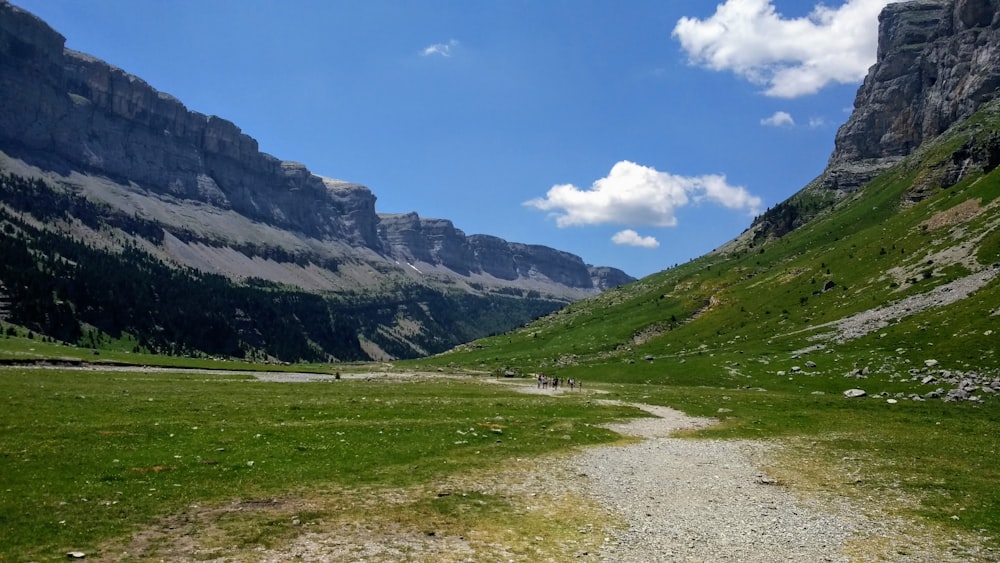 green grass field near mountain under blue sky during daytime