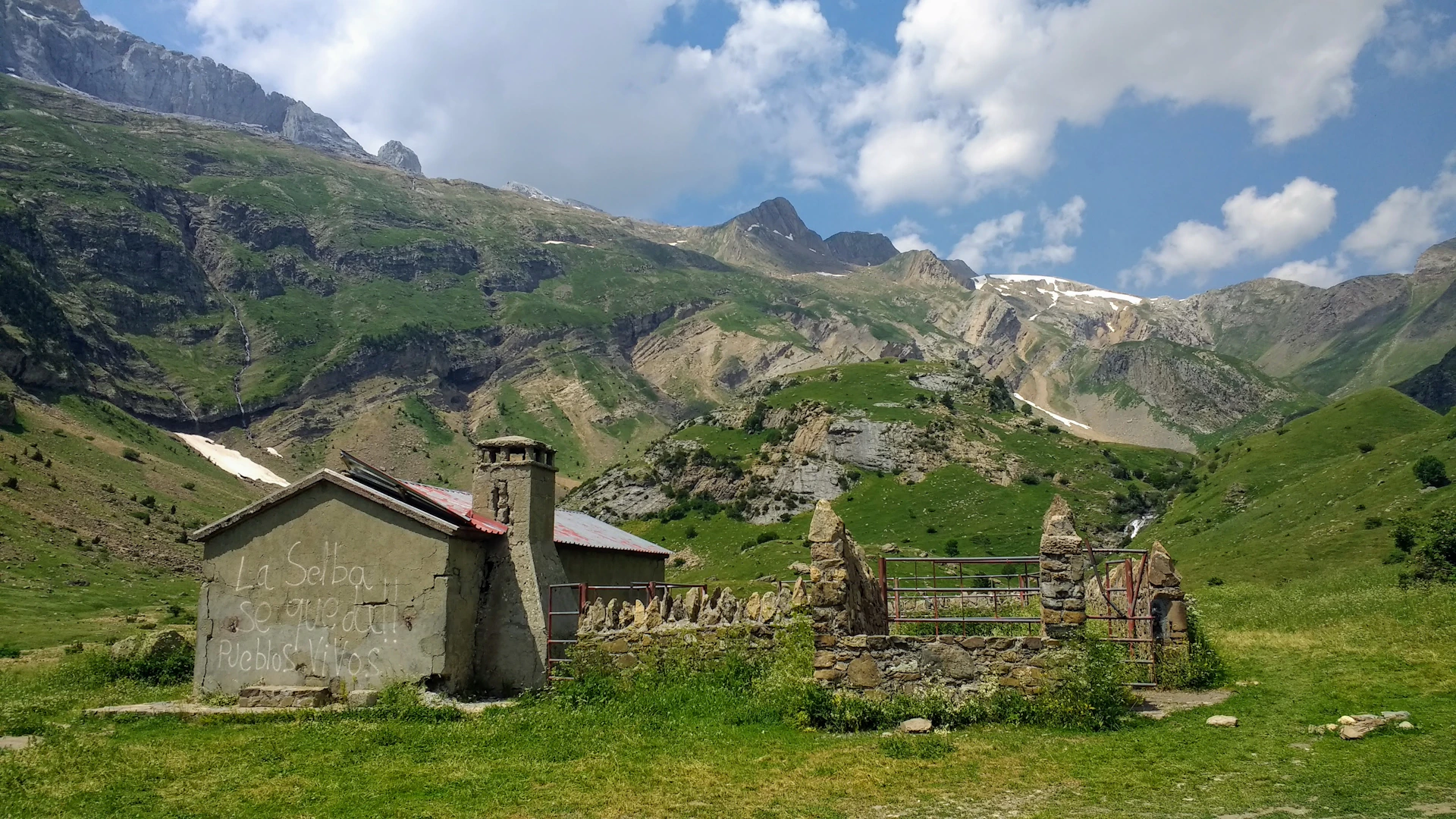 gray concrete house on green grass field near mountain under white clouds during daytime