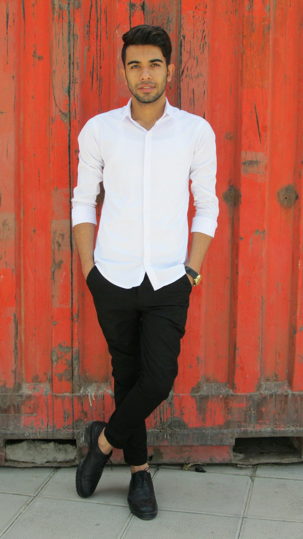 man in white dress shirt and black pants standing beside red wooden door