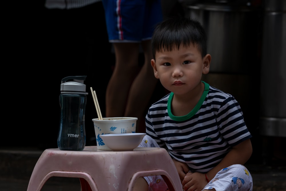 boy in black and green striped crew neck t-shirt sitting on red plastic chair