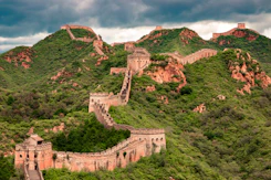 The Great Wall of China winding over green mountain ridges under a cloudy sky