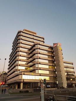 A sleek modern office building illuminated with gold accents at dusk, reflecting the premium property investment focus of Rayuna Investama.