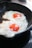 Two fried eggs with vividly orange yolks are sizzling in a cast iron skillet. The edges of the whites are bubbly and slightly crispy, indicating they are being cooked over heat.