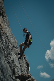 man in black tank top and black shorts climbing on gray rocky mountain during daytime