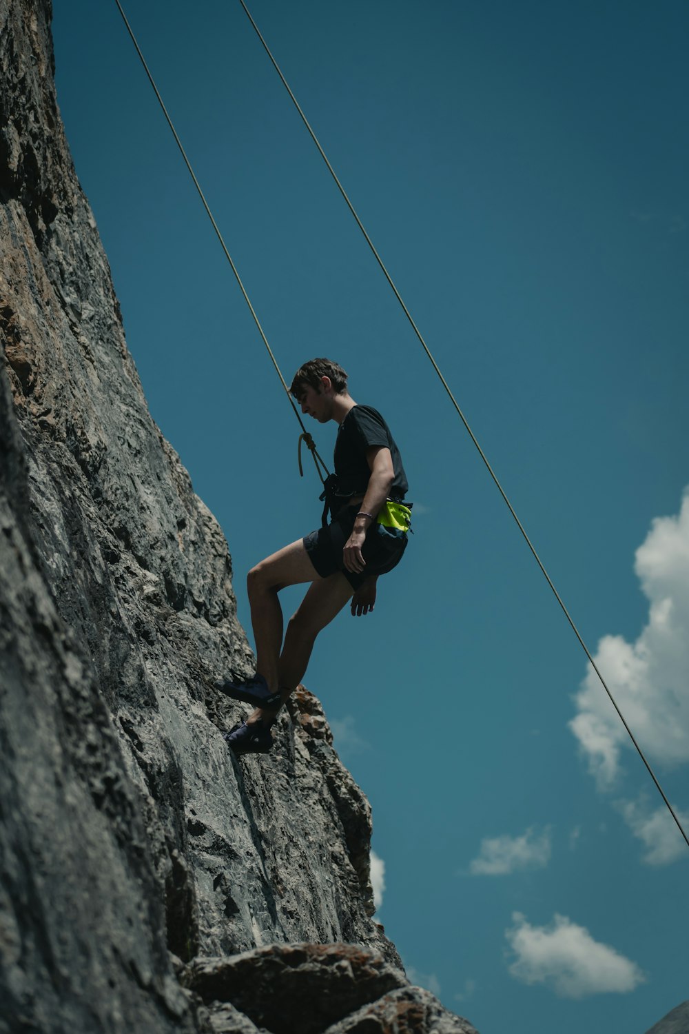 man in black tank top and black shorts climbing on gray rocky mountain during daytime