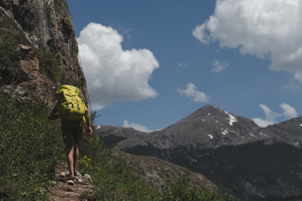 man in yellow shirt and black shorts standing on rocky mountain under white clouds and blue