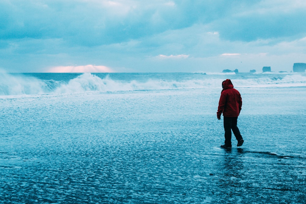 man in red jacket standing on sea shore during daytime