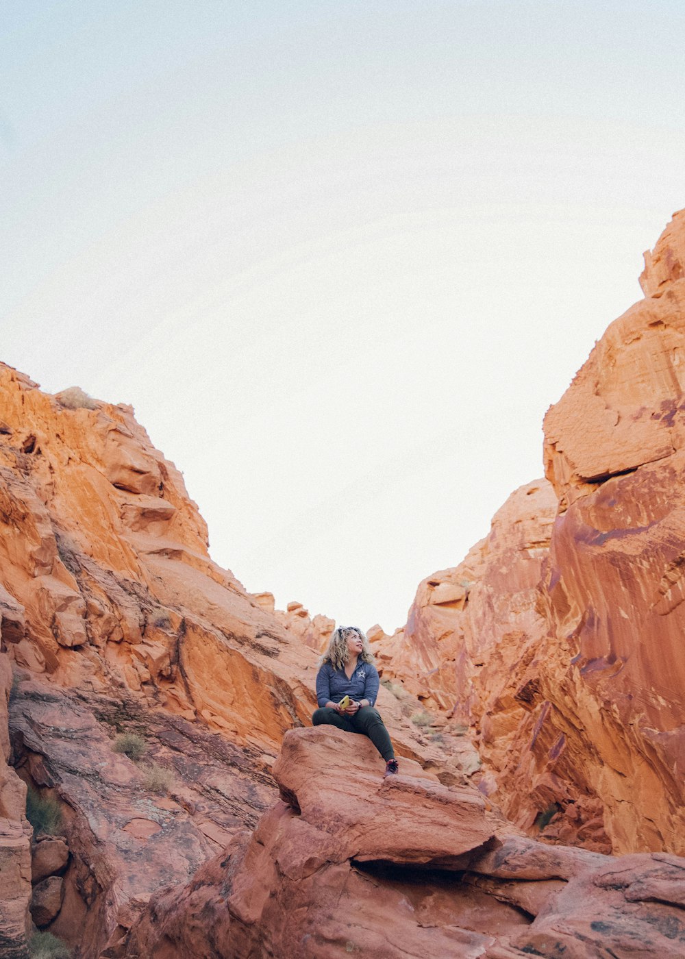 man in blue jacket and black pants sitting on brown rock formation during daytime
