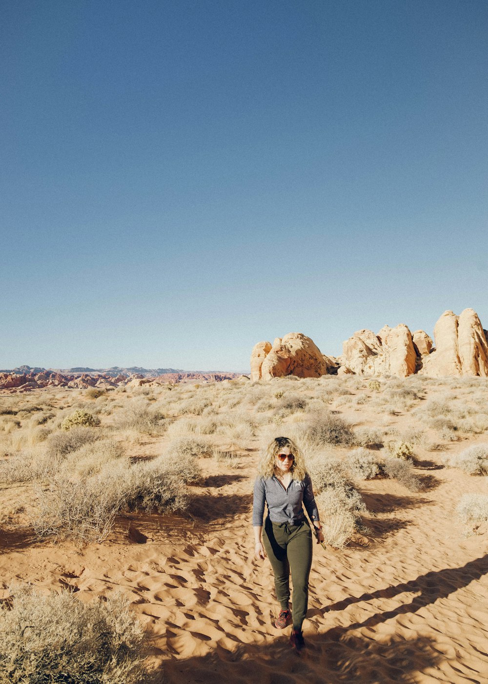 woman in gray long sleeve shirt standing on brown sand during daytime