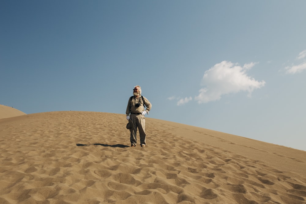 Frau in brauner Jacke und schwarzer Hose, die tagsüber auf braunem Sand spazieren geht