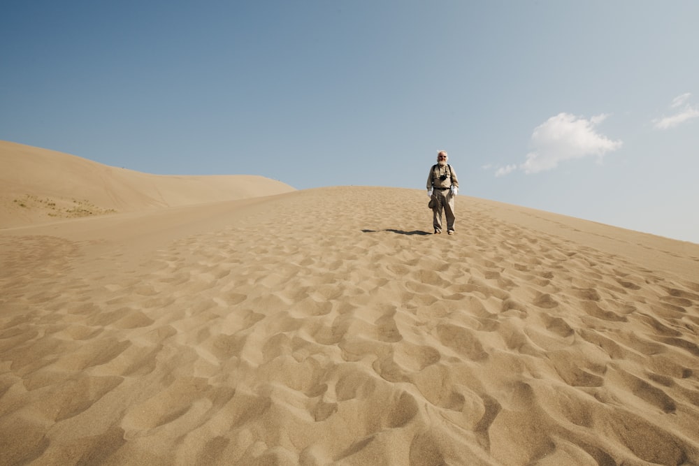 uomo in giacca nera che cammina sul deserto durante il giorno