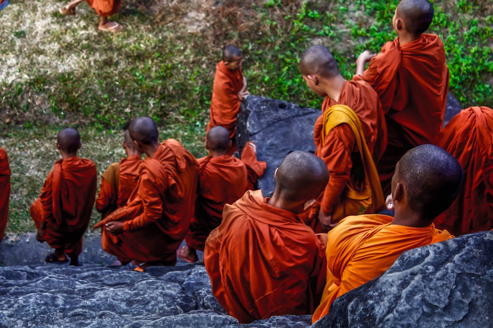 boys in orange robe sitting on gray rock during daytime