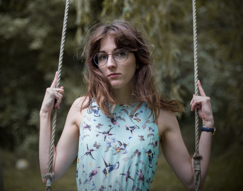 woman in blue and white floral tank top wearing brown sunglasses sitting on swing during daytime