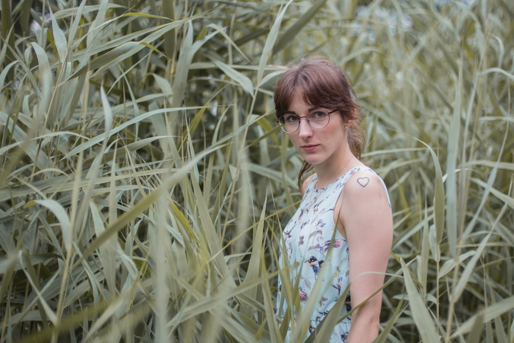 woman in white and blue floral sleeveless dress standing on green grass field during daytime