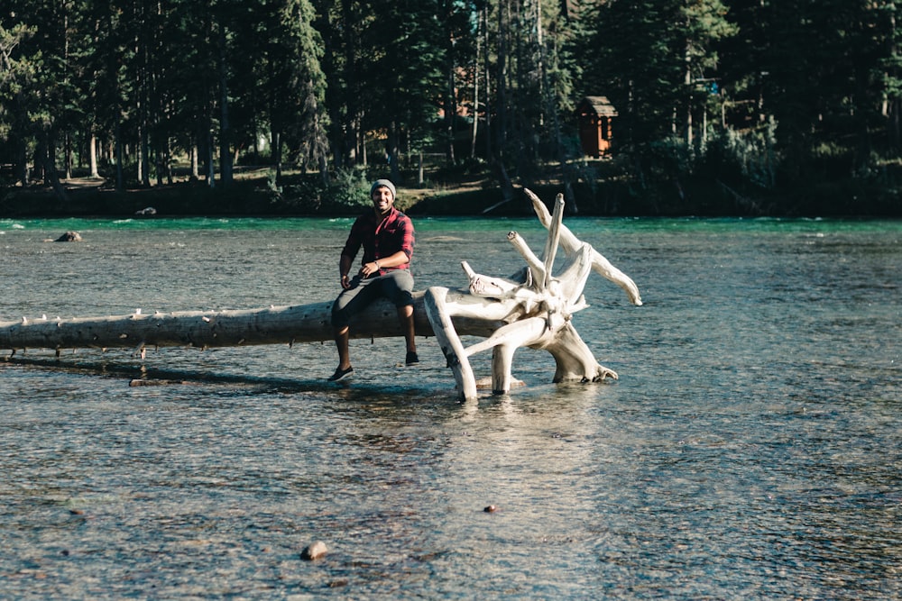 man in black shirt sitting on tree log on water during daytime