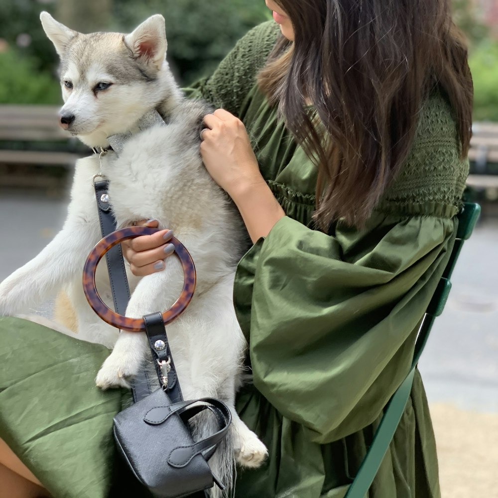 woman in green jacket holding white short coat dog