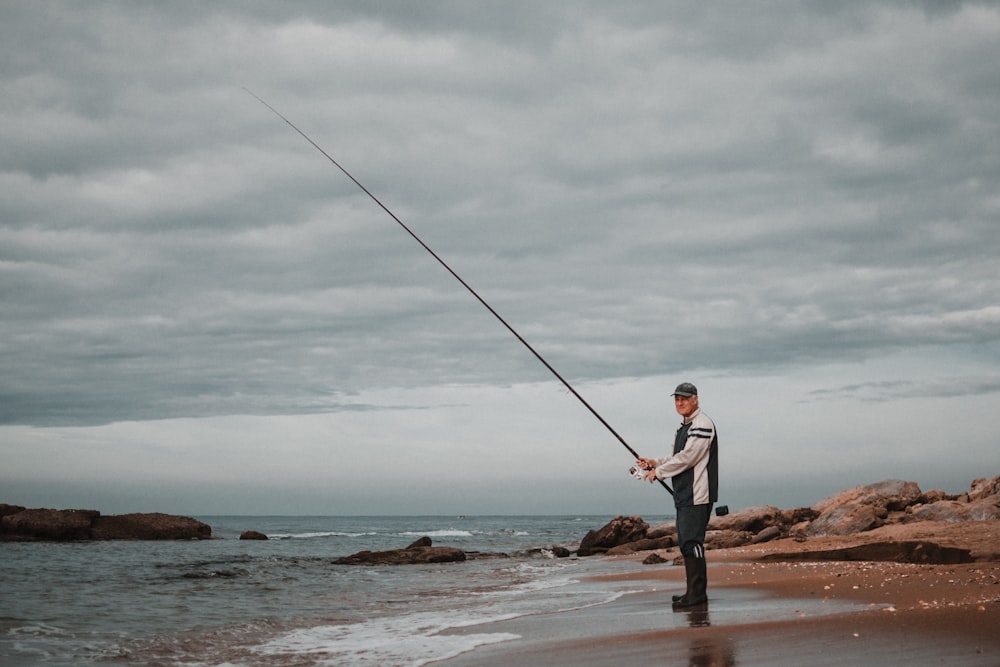 man in white shirt and brown pants fishing on sea shore during daytime