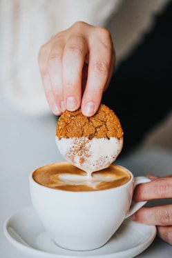 person holding white ceramic mug with brown and white liquid