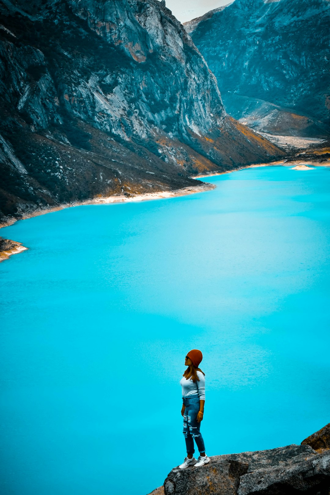 man in white shirt standing on blue lake near brown mountains during daytime