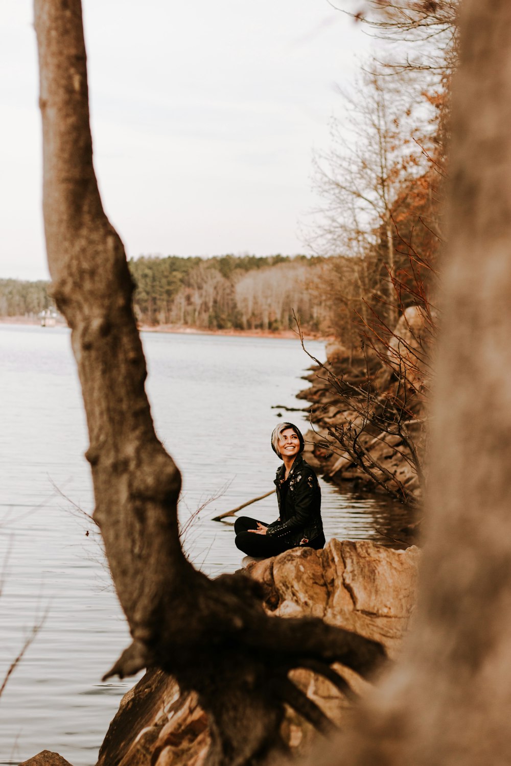 man in black jacket sitting on brown rock near body of water during daytime