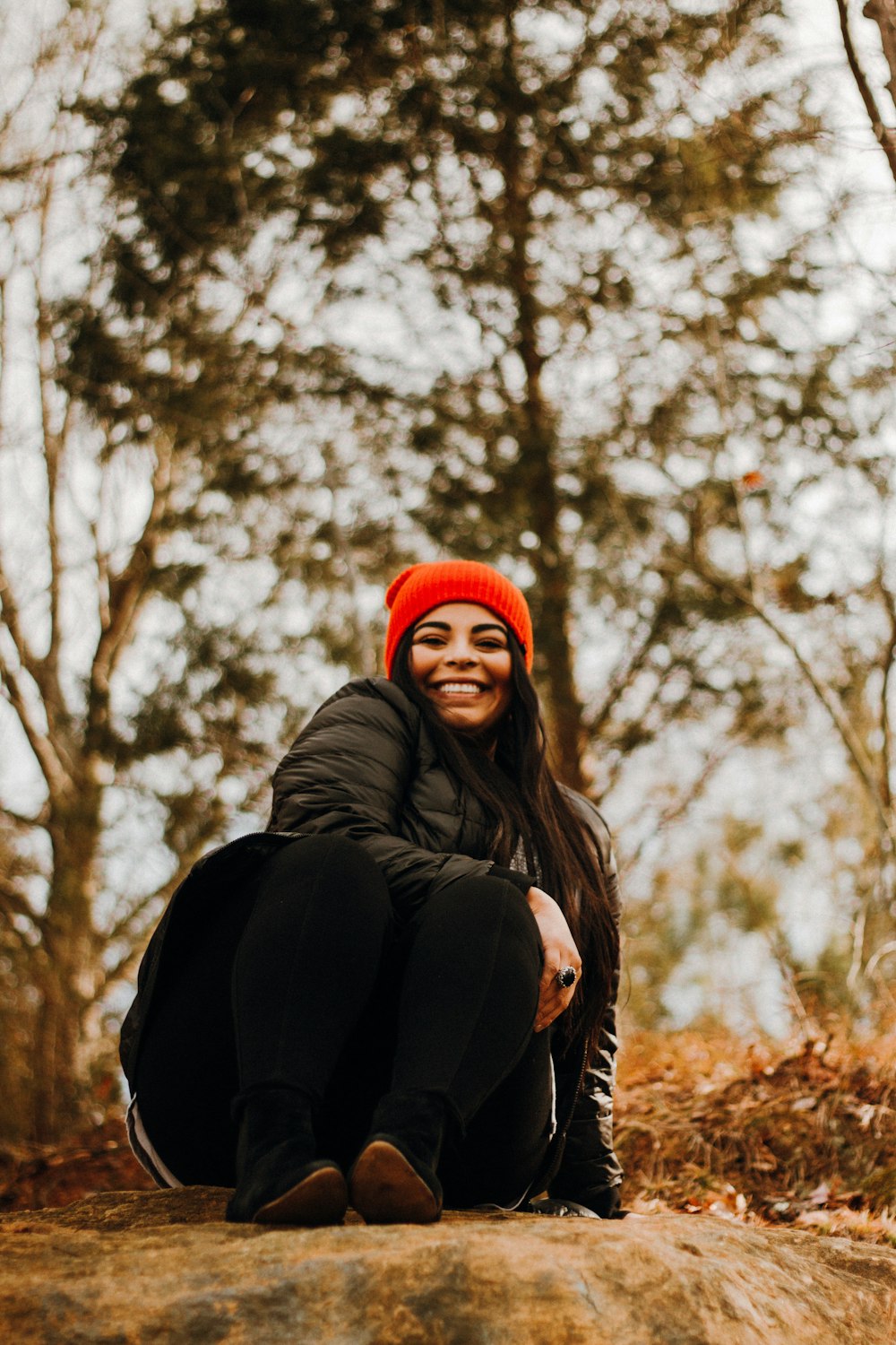 woman in black jacket and red knit cap sitting on ground under white sky during daytime