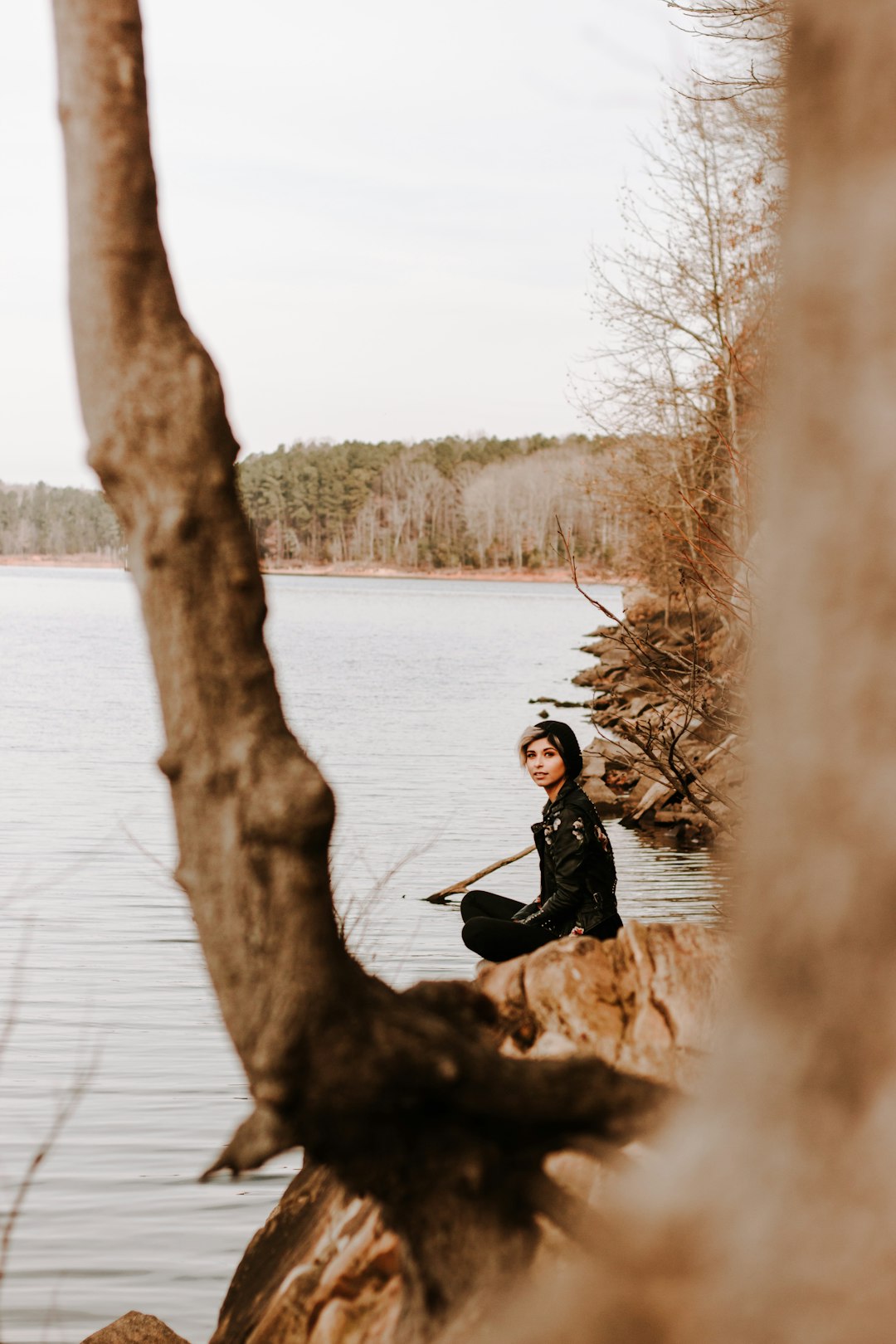 man in black jacket sitting on brown tree log on lake during daytime
