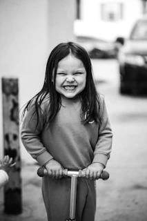 A smiling child riding a small, bright scooter in a sunny park.