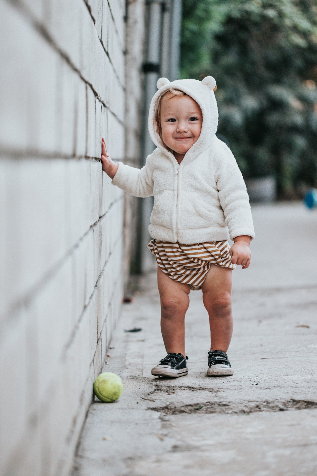 girl in white hoodie and brown and white polka dots skirt holding green tennis ball