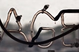 A close-up view of a neon sign with a portion of the letters 'AGE' visible. The neon tubes are unlit, with wiring and connectors attached. The background appears blurred, possibly showing an outdoor scene.