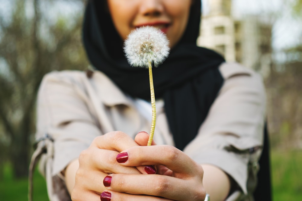 person in black hijab holding white dandelion flower