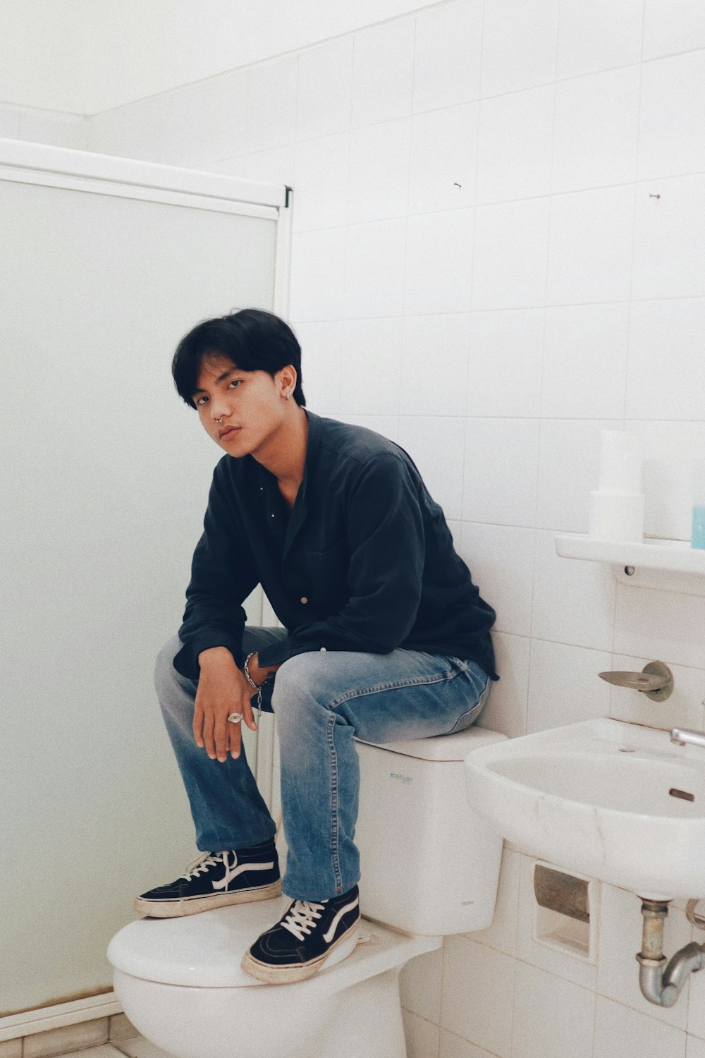 man in blue dress shirt and blue denim jeans sitting on white ceramic toilet bowl