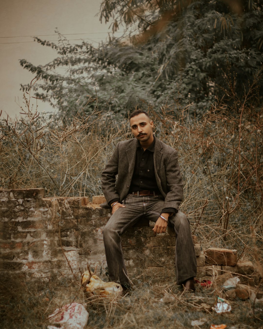 man in black jacket sitting on brown concrete brick wall during daytime