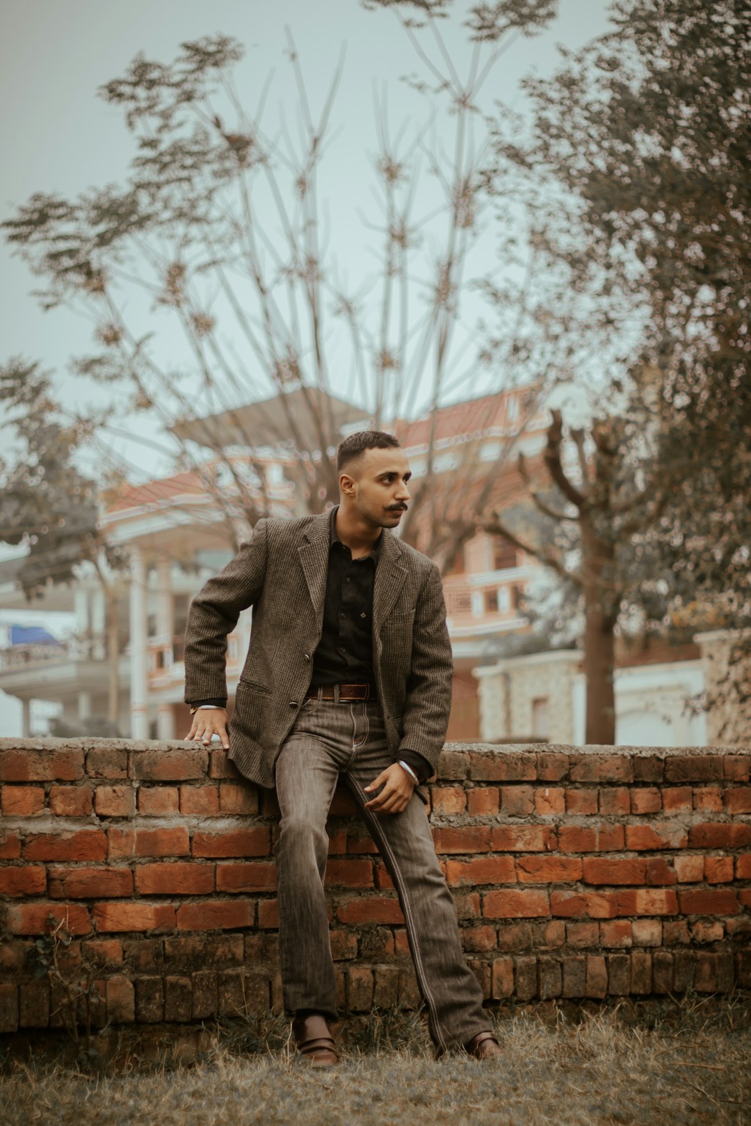 man in gray coat sitting on brown brick wall during daytime