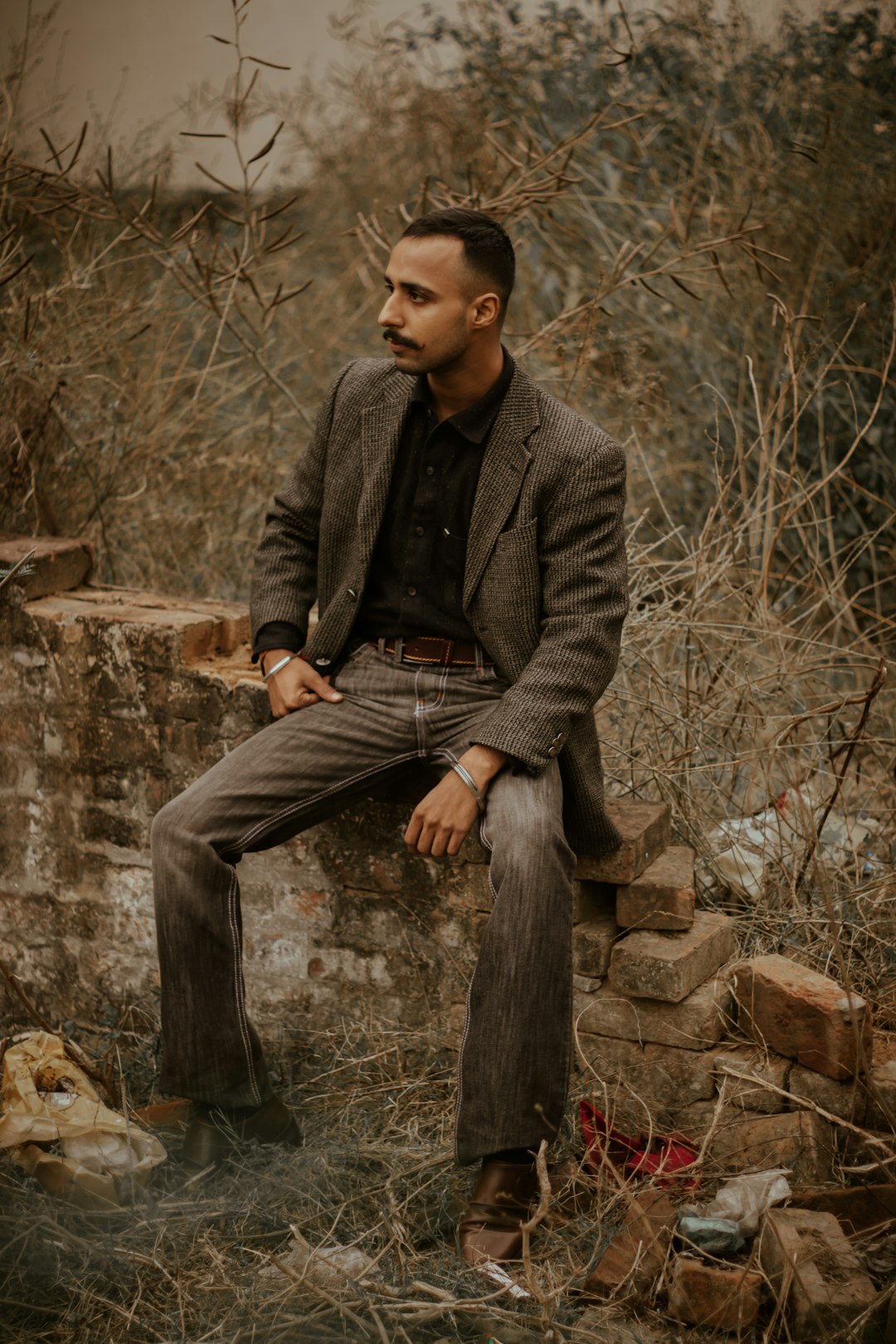 man in gray suit jacket and black pants sitting on brown rock