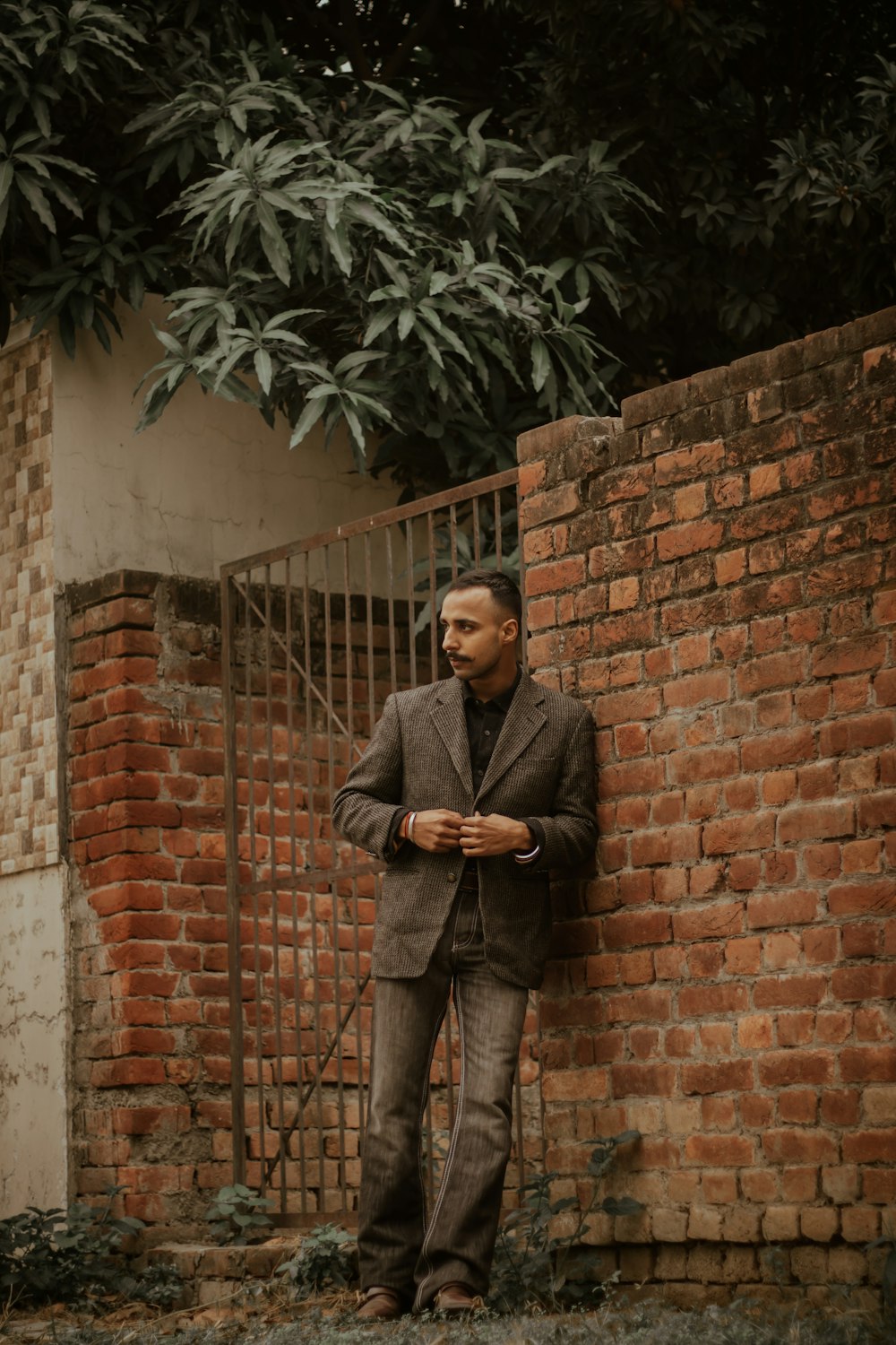 man in black suit standing beside brown brick wall