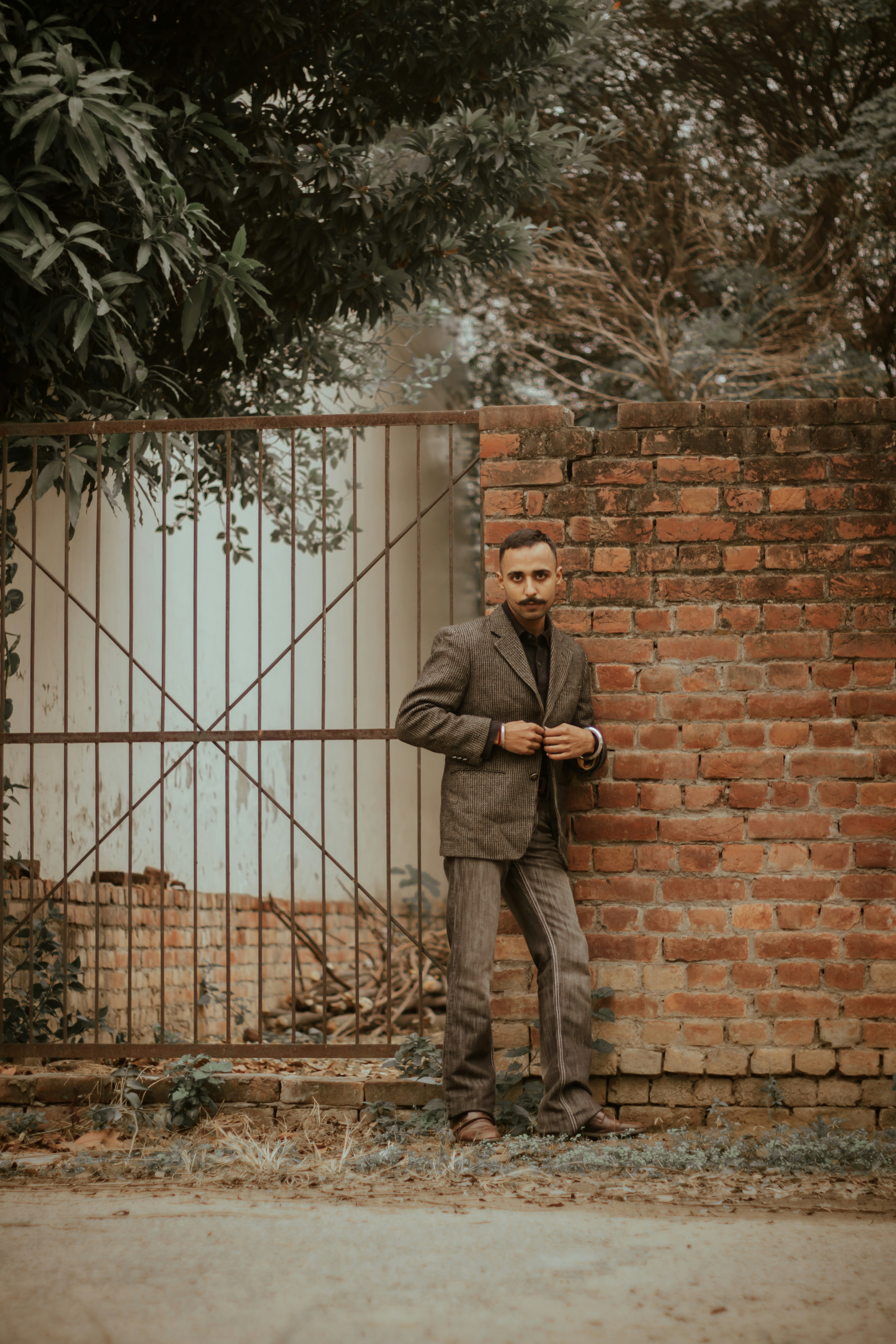 man in gray suit standing beside brown brick wall