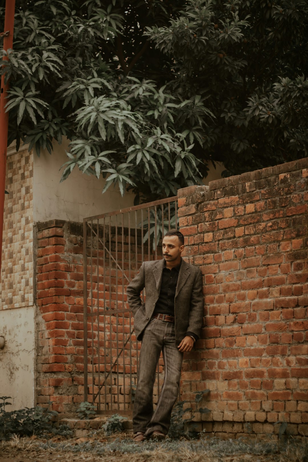 man in gray suit jacket and gray pants standing beside brown brick wall